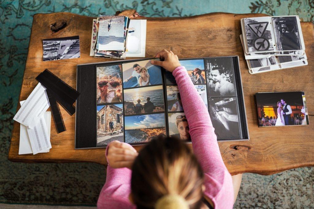 młoda dorosła kobieta dodająca zdjęcia do albumu fotograficznego w domu